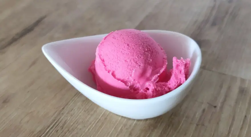 Ein Löffel leuchtend pinkes Eis in einer weißen Schale. Vielleicht ist das die Antwort auf die Frage, warum es kein Kirscheis gibt – weil dieses hier so gut ist!