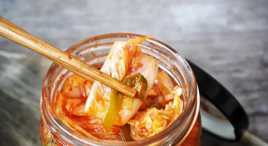 Pałeczki bambusowe wyciągają kawałek kimchi z słoika.