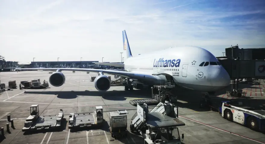 Lufthansa A380 na płycie lotniska we Frankfurcie. W tle widać inne samoloty i budynki terminali, typowe dla lotnisk w Niemczech.