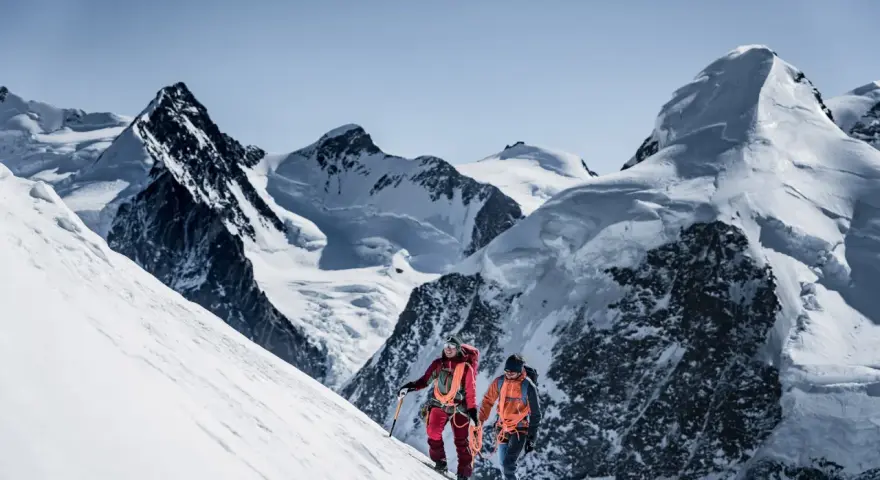 Zwei Bergsteiger, ein beal escaper-Team, steigen einen schneebedeckten Hang hinauf, umgeben von majestätischen, eisigen Gipfeln.