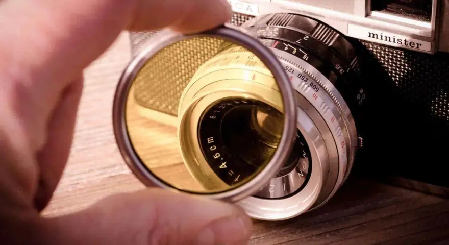 Une main tient un filtre protection objectif devant un vieil appareil photo argentique.