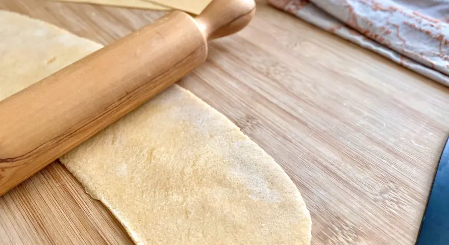 Mit einem Nudelholz wird Teig für **ravioli selber machen ohne maschine** auf einem Holzbrett ausgerollt.