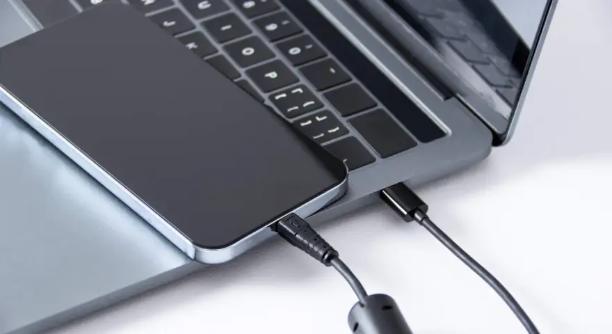 Ein iPhone wird über ein USB-C-Kabel mit einem Laptop verbunden, um Fotos zu übertragen.