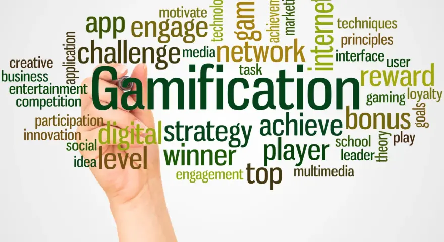 Ręka pisze słowo "Gamification" otoczone chmurą powiązanych terminów, takich jak "gra", "nagroda", "bonus", "strategia", "motywacja" i "sieć". Grywalizacja w akcji!