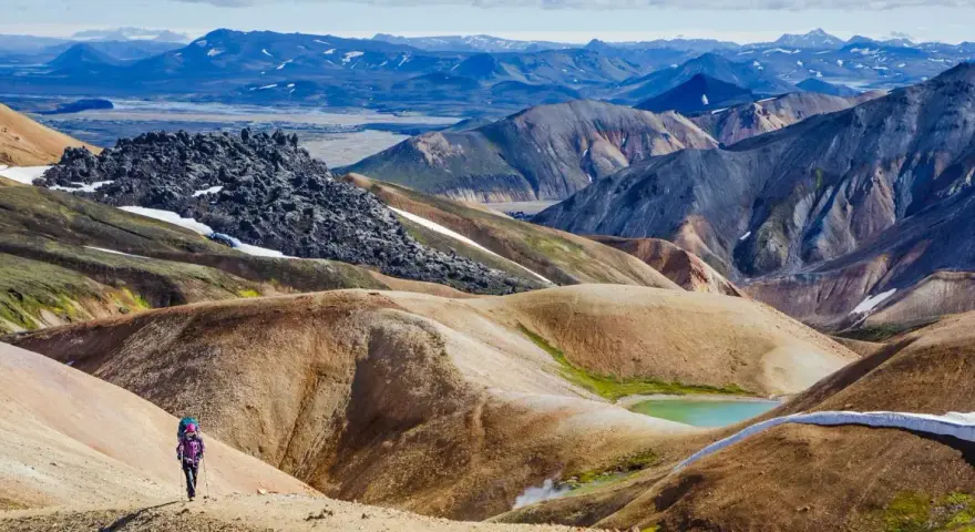Un randonneur solitaire explore les paysages colorés et volcaniques de Landmannalaugar, un trek inoubliable en Islande.