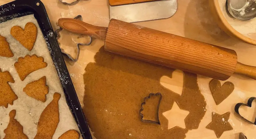 Pepparkaksdeg recept förbereds med kavel och pepparkaksformar. Färdiga pepparkakor ligger på en plåt.