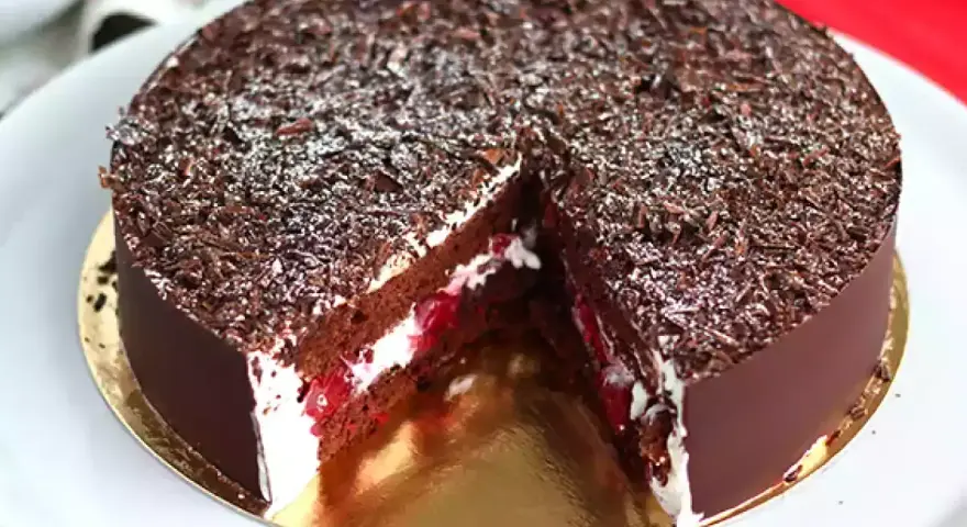 Tarta Selva Negra, con capas de bizcocho de chocolate, nata montada y cerezas, cubierta de virutas de chocolate y un toque de azúcar glas.