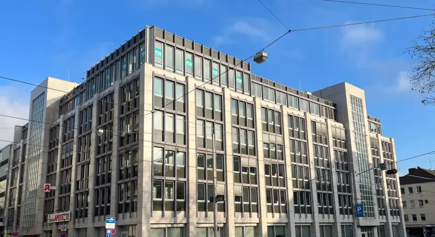 Modernes Bürogebäude in Kassel mit vielen Fenstern und "FOM"-Logos. Eine Apotheke ist im Erdgeschoss sichtbar.