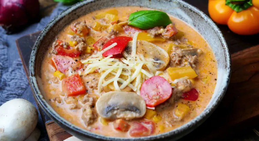 Herzhaftes pizzasuppe rezept mit Hackfleisch, Paprika, Mais und Pilzen, garniert mit Käse und Basilikum.