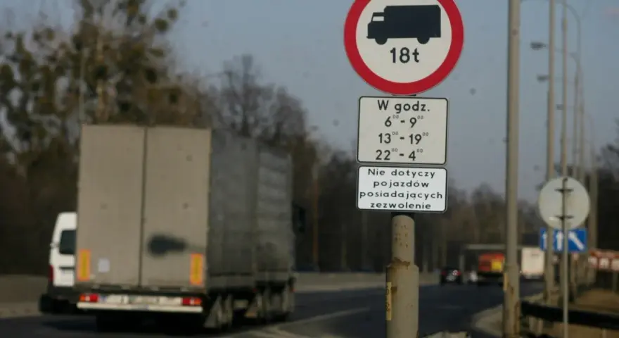 Znak zakazu wjazdu dla ciężarówek powyżej 18t w określonych godzinach. Czy ciężarówki mogą jeździć w niedzielę? Ten znak wyjaśnia ograniczenia.
