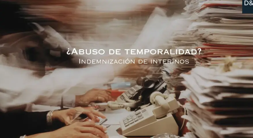 ¿Abuso de temporalidad? Indemnización de interinos tras 3 años. Escritorio caótico con papeles y teléfonos.