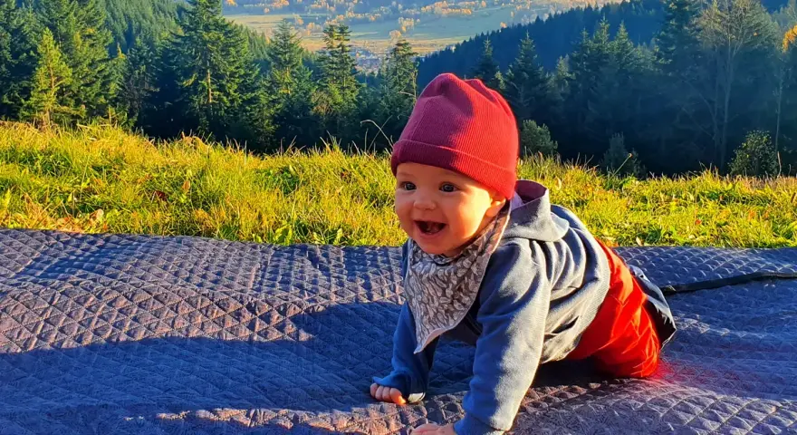 Uśmiechnięte dziecko na kocyku, w tle góry i las. Jakby czytało psalm 131 tekst o spokoju.