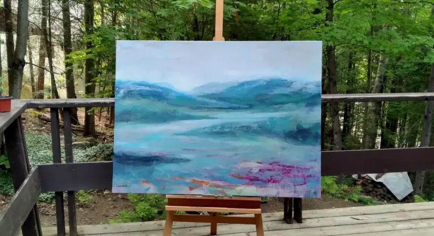 Un paysage abstrait aux teintes bleues et vertes, évoquant des montagnes brumeuses et un lac. Le fond de tableau peinture est posé sur un chevalet, en extérieur, entouré de verdure.