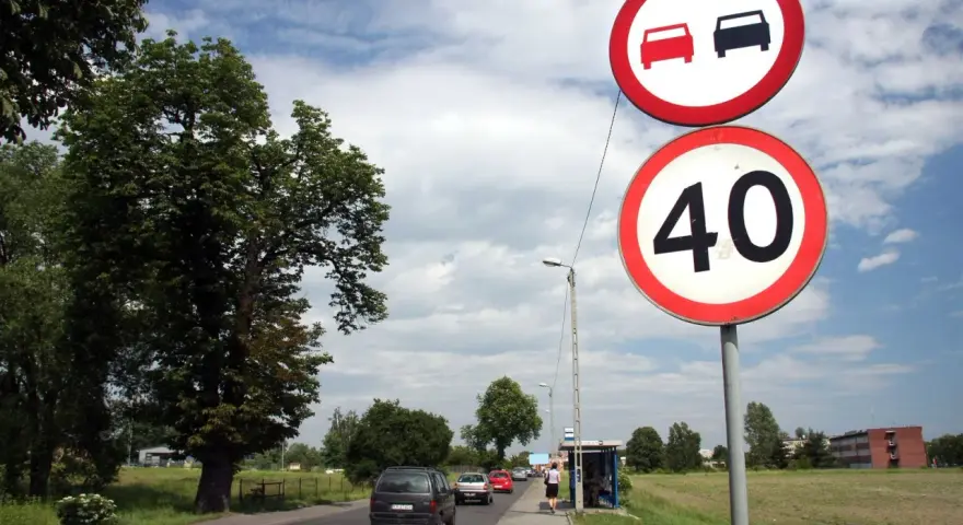 Znaki drogowe: zakaz wyprzedzania i ograniczenie prędkości do 40 km/h. Droga z samochodami i drzewami.