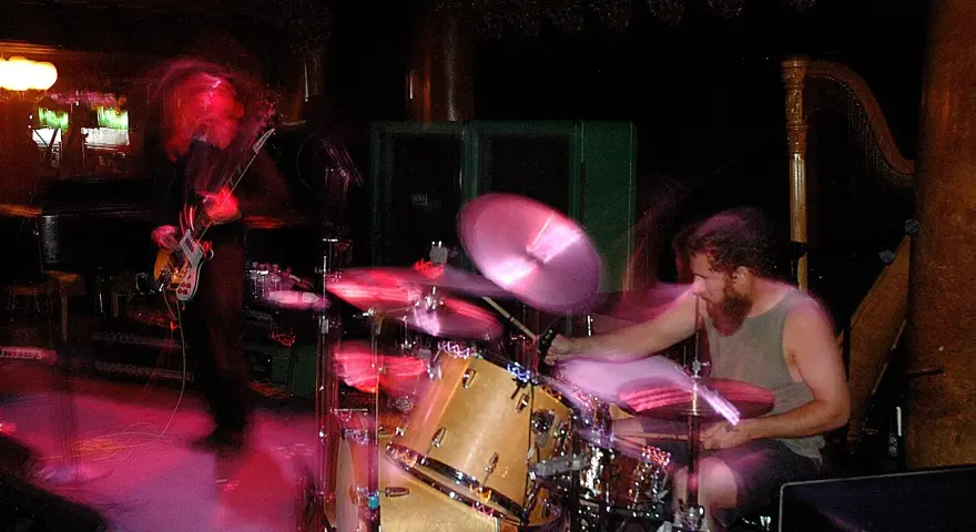 Ein Bassist und ein Schlagzeuger einer Stoner Rock Band in Aktion. Die Lichter und Bewegungen erzeugen eine dynamische Atmosphäre.
