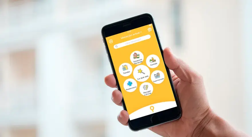 Mano sujetando un smartphone con una app de entregas. Muestra opciones como "Comida", "Supermercado" y "Parafarmacia". Así funciona "just eat".