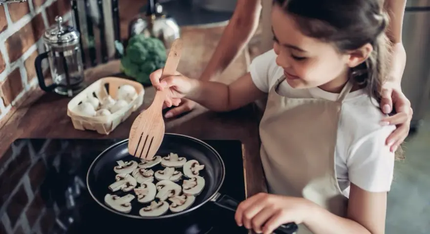 Mała kucharka smaży pieczarki na patelni. Czy dzieci mogą jeść pieczarki? Tak, to zdrowy dodatek do posiłków!