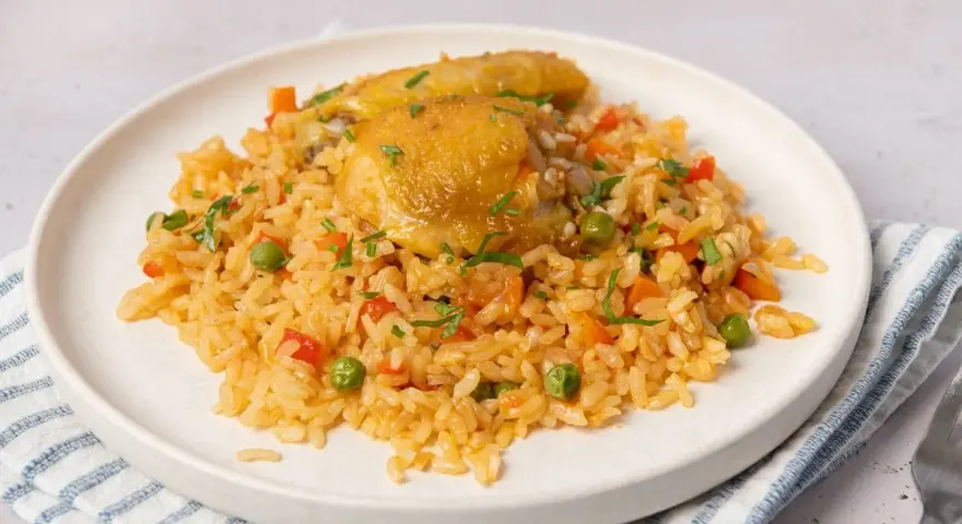 Arroz con pollo jugoso con verduras y perejil picado en un plato blanco.