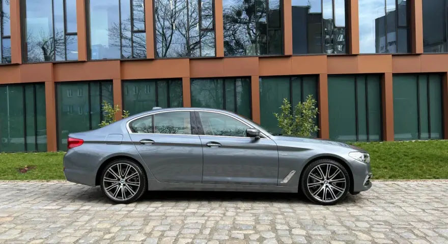 Szary sedan BMW G30 na tle nowoczesnego budynku.