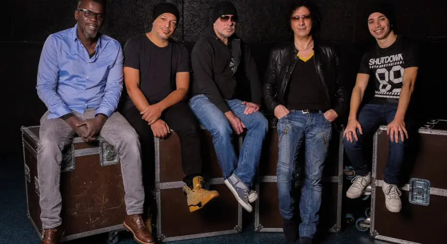 Les membres de Trust (groupe) posent ensemble, assis sur des flight cases, prêts pour leur prochaine performance.