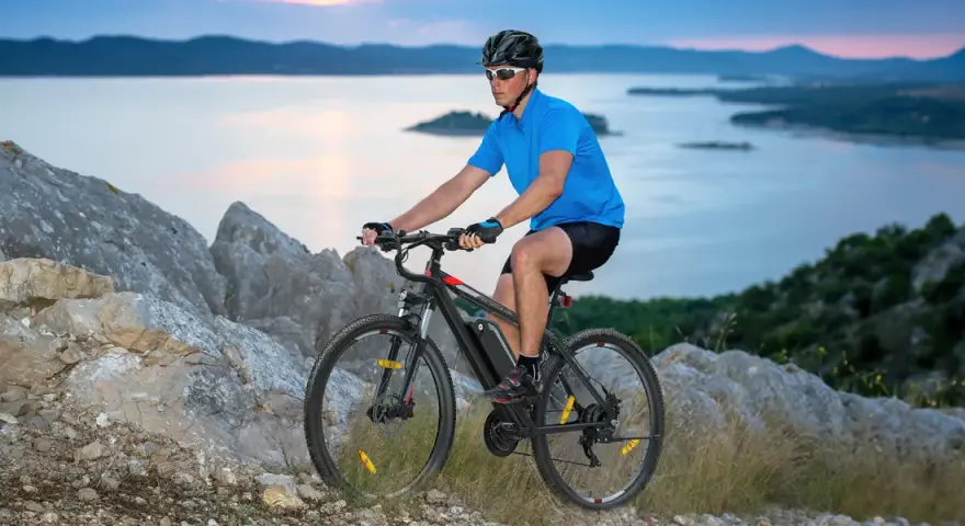 Man riding a mountain bike on a rocky trail overlooking a serene bay at dusk.