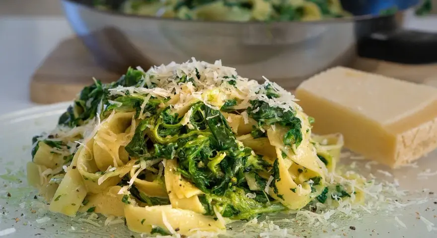 Makaron tagliatelle ze szpinakiem i startym parmezanem, obok kawałek sera.