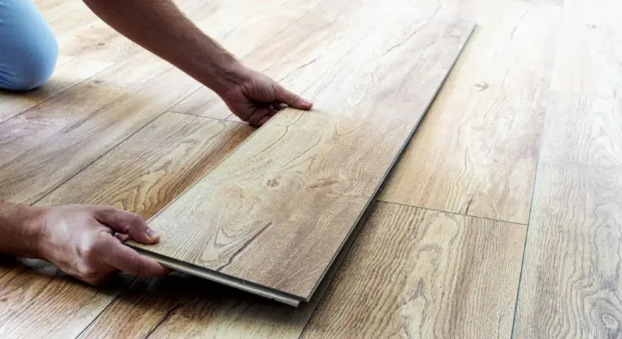 Man's hands placing a laminate plank to repair suelo laminado.