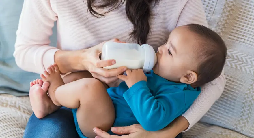 Mama karmi dziecko butelką. To przykład karmienia mieszanego, gdzie dziecko otrzymuje zarówno mleko matki, jak i mleko modyfikowane.