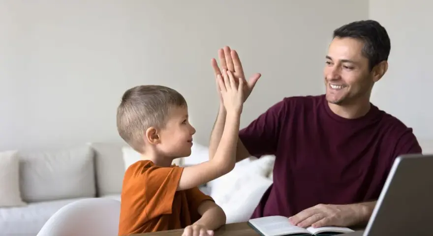 Ojciec i syn dają sobie piątkę, świętując sukcesy w nauce. To chwila radości, kiedy nie stawiamy przecinka, bo wszystko jest jasne.