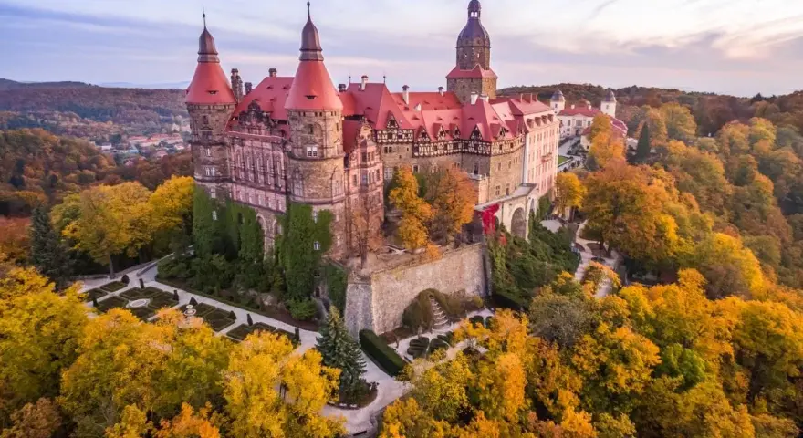 Zamek Książ otoczony jesiennym lasem, z widoczną palmiarnią w oddali.