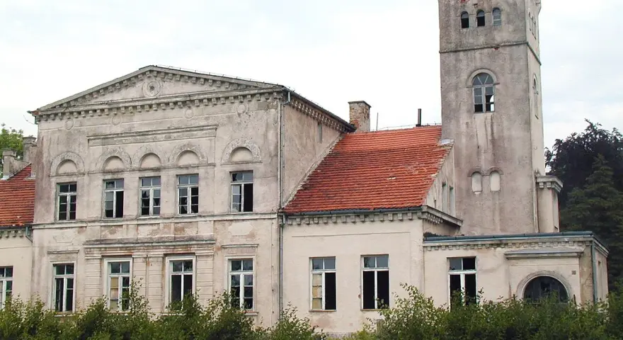 Pałac Rekowo, z wieżą i czerwoną dachówką, otoczony zielenią.