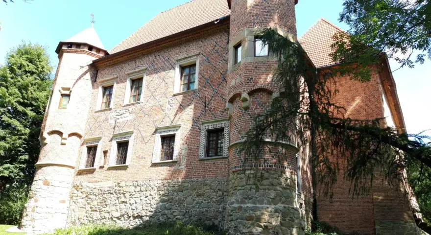 Zamek w Dębnie Polskim, ceglana budowla z kamiennym cokołem, otoczona zielenią.