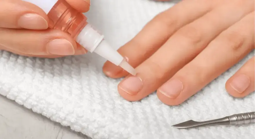 Application d'huile sur les cuticules des ongles pour un soin hydratant. Un petit pinceau dépose le produit sur le contour de l'ongle.
