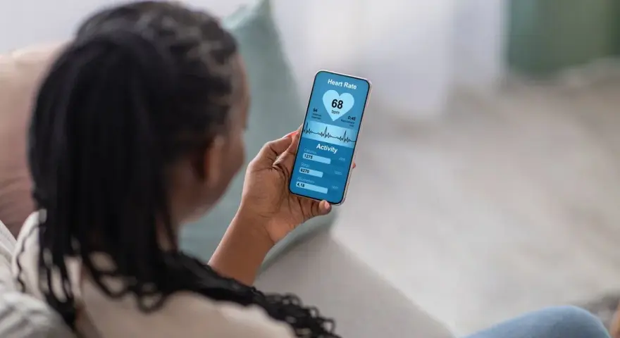 Kobieta sprawdza na telefonie swoje skoki tętna i aktywność fizyczną. Widzi 68 uderzeń na minutę, spalone kalorie i pokonane kroki.