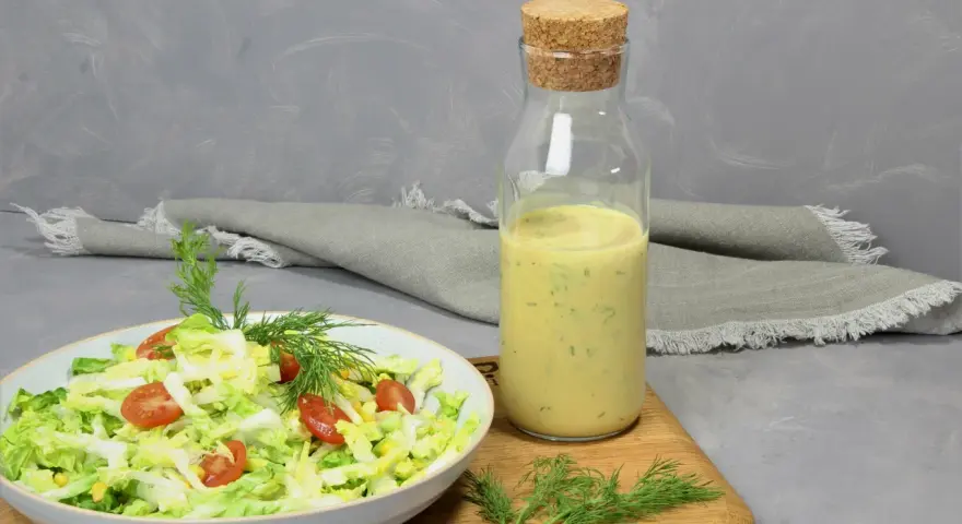 Frischer Salat mit Tomaten und Mais, daneben eine Flasche mit cremigem Jogurt Dressing und Dill.