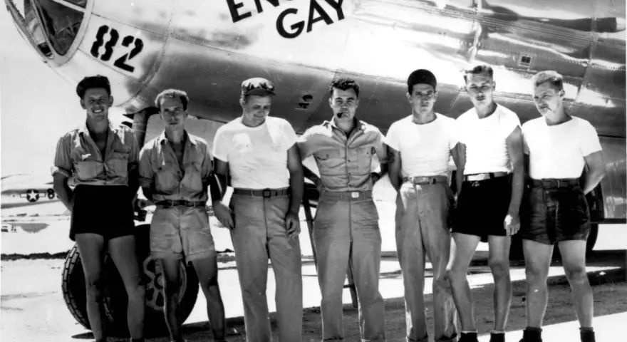 Siedmiu mężczyzn pozuje przed samolotem B-29 o nazwie "Enola Gay".
