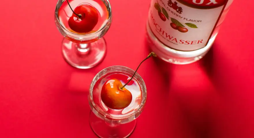 Zwei Gläser mit Kirschen und eine Flasche Kirschwasser auf rotem Hintergrund. Was ist Cherry? Ein süßer Genuss.