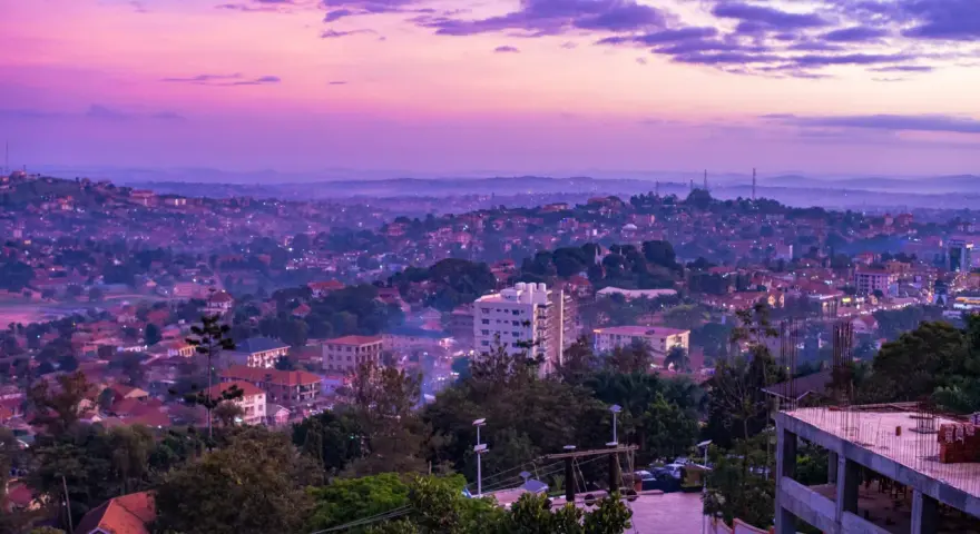 Fioletowe niebo nad krajem z kampalą, z widokiem na wzgórza pokryte zabudowaniami i zielenią.