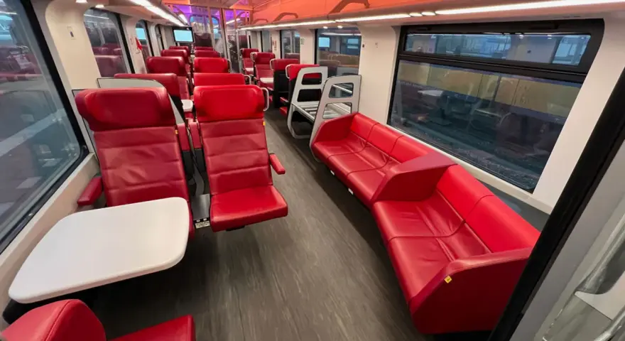 Interior of a modern train, with red leather seats and tables, ready for a journey from AMS to Brussels.