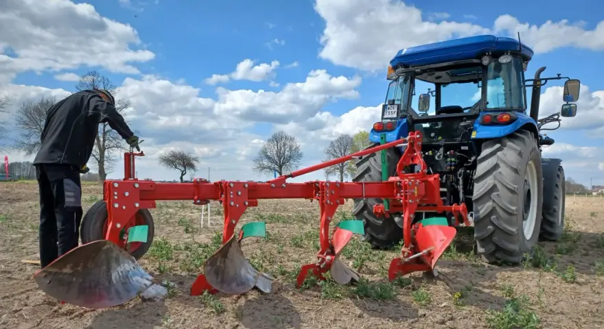 Rolnik przygotowuje pług do orania ziemi. Błękitne niebo z chmurami nad polem.