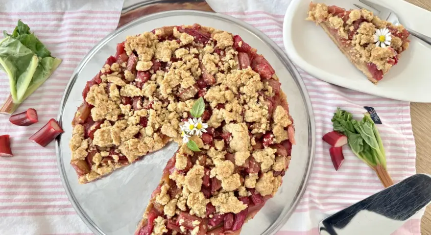 Ein köstlicher Rhabarberkuchen mit Streuseln, garniert mit Gänseblümchen. Frischer Rhabarber und knusprige Streusel machen diesen Kuchen zum Genuss.