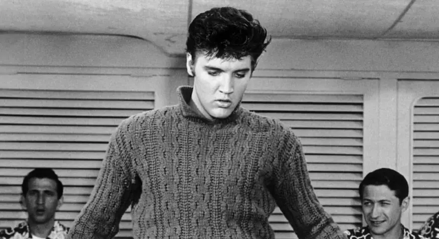 Elvis Presley in einem Strickpullover, vielleicht bei der Aufnahme seines letzten Liedes. Im Hintergrund zwei Männer.