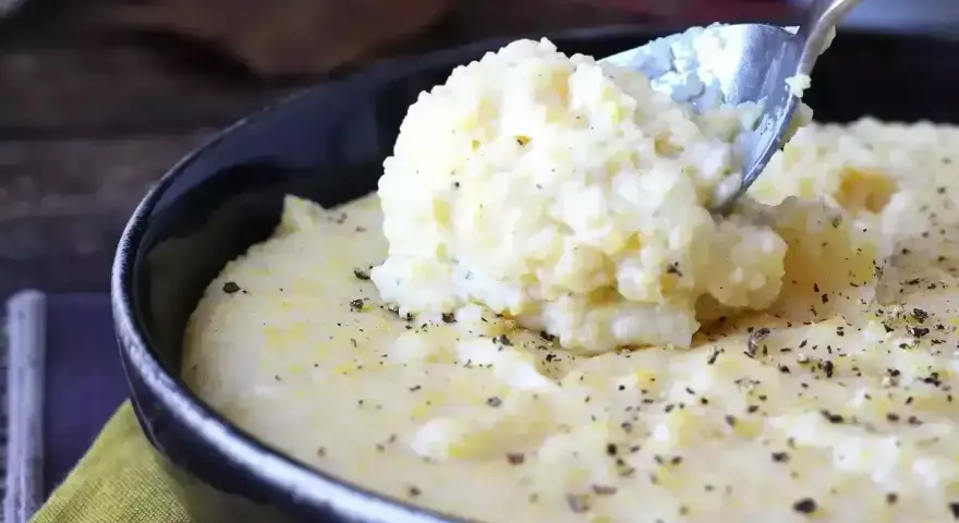 Kremowa polenta, idealna do prostego polenta przepis, posypana świeżo mielonym pieprzem, nabierana łyżką z czarnej miski.