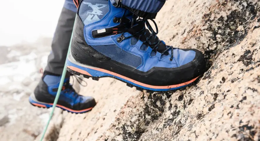 Close-up of a blue and black hiking boot with orange accents, gripping a rocky surface.