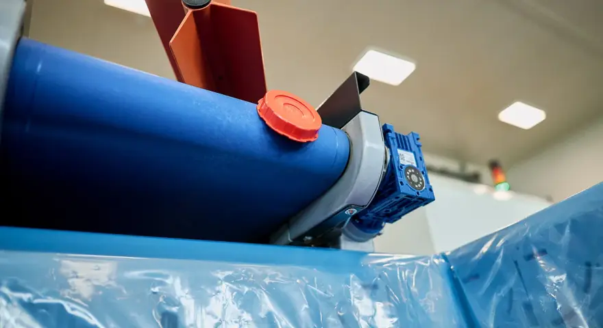 Maszyna do produkcji folii, z niebieskim wałkiem i pomarańczową nakrętką, przygotowuje materiał cerplast do dalszej obróbki.