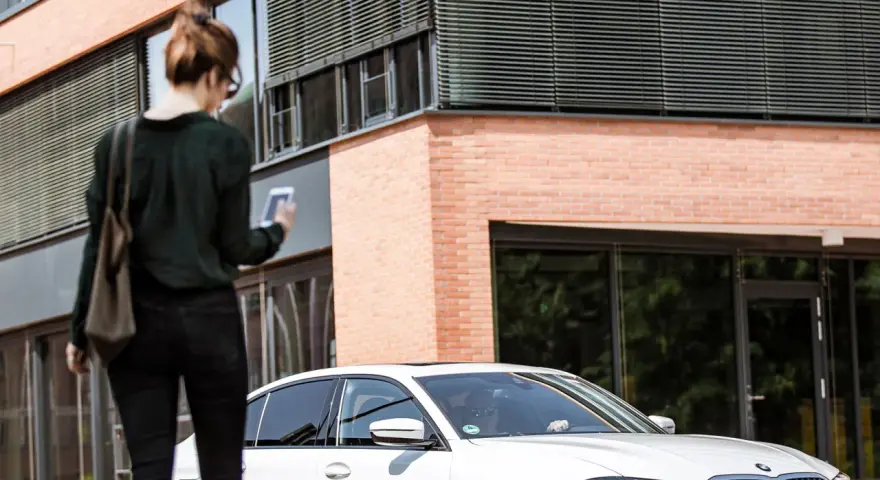 Frau mit Smartphone wartet auf FREE NOW Fahrt. Keine Beschwerde, nur Vorfreude auf die Fahrt.