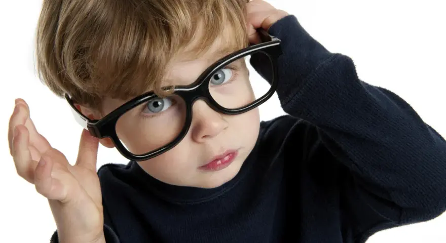Chłopiec z niebieskimi oczami poprawia okulary, zastanawiając się nad nadwzrocznością u dzieci kiedy okulary są potrzebne.