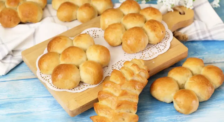 Morbidi panini al latte dorati, alcuni disposti a grappolo su un tagliere, altri su un panno bianco.