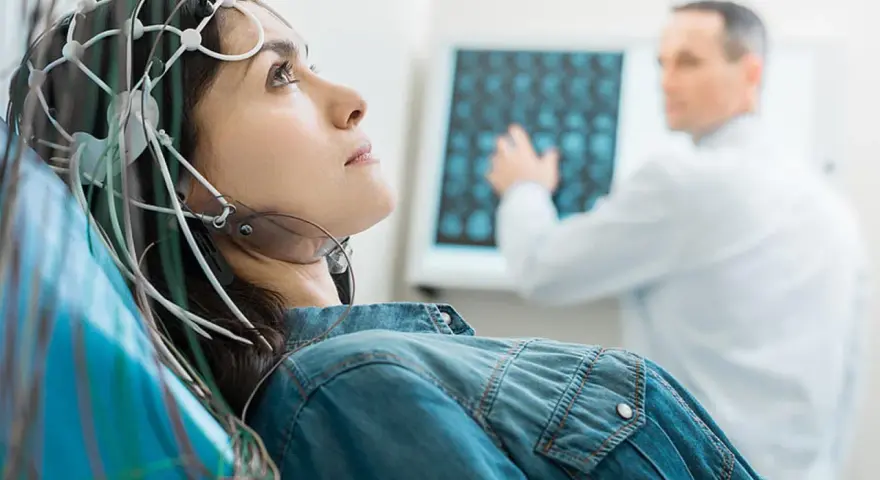 Frau mit EEG-Kappe für eeg medizinische Untersuchung, Arzt deutet auf Bildschirm mit Gehirnscans.