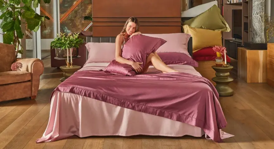Una donna sorride su un letto con lenzuola rosa. Per mantenerle fresche, si lavano a 40 gradi.
